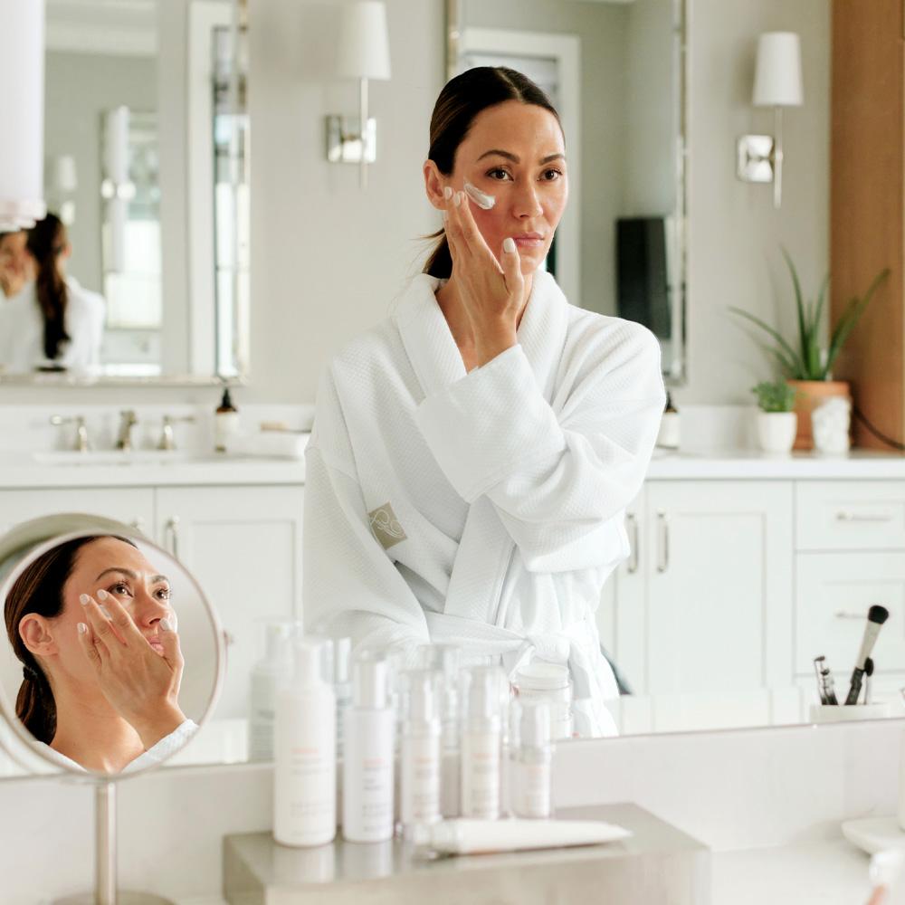 Woman wearing Panama robe in bathroom putting face cream